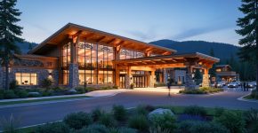 Modern Indigenous-owned casino resort at dusk with cedar-and-stone facade, subtle tribal-inspired motifs, warm interior lights, and forested hills in the background.