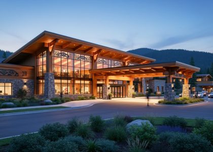 Modern Indigenous-owned casino resort at dusk with cedar-and-stone facade, subtle tribal-inspired motifs, warm interior lights, and forested hills in the background.
